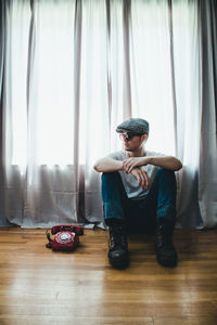 Young man sitting by rotary phone on hardwood floor at home