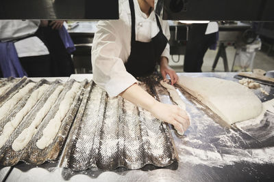 Midsection of female chef shaping raw breadstick in commercial kitchen