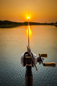 Fishing rod over sea against clear sky during sunset