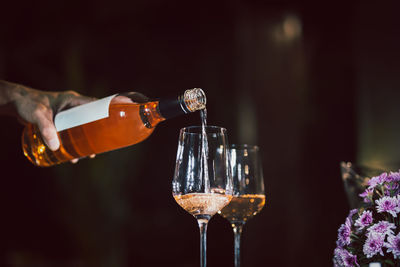 Man pouring rose wine from bottle into glass indoors.