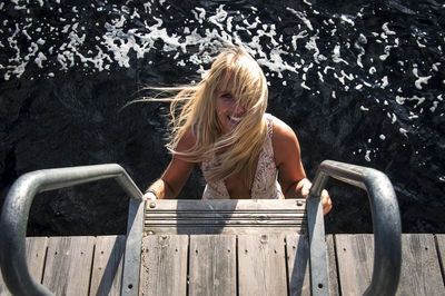 Portrait of smiling young woman standing on steps against sea