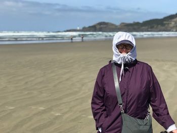 Portrait of mature woman wearing warm clothing while standing on sand at beach