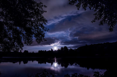 Silhouette trees by lake against sky at night