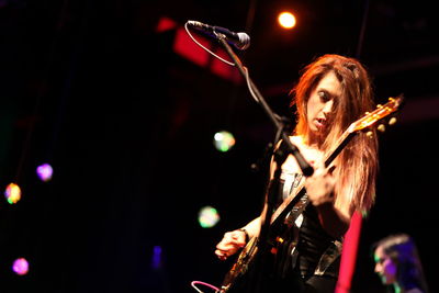 Young woman playing guitar at music concert