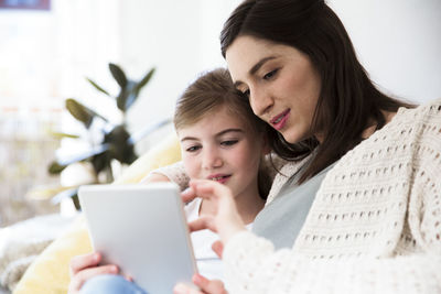 Smiling mother and daughter at home using tablet