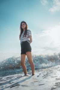 Full length portrait of young woman standing against sky