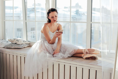 Ballet dancer using mobile phone while sitting at window