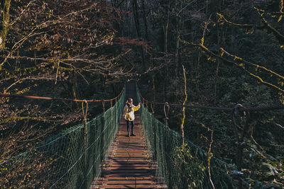 Rear view of woman walking on footbridge in forest