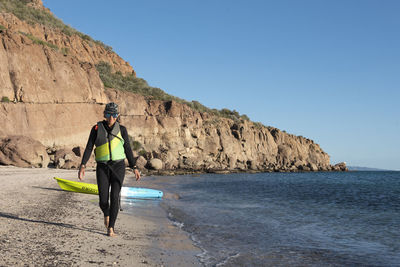 A woman wearing a wetsuit walking on the beach after kayaking in carmen island, loreto, baja california, mexico.