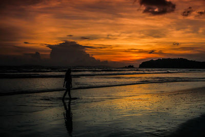 Silhouette person on beach against sky during sunset