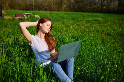 Young woman using digital tablet while sitting on grassy field