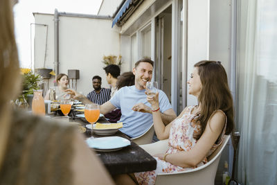 Happy male and female multiracial friends enjoying drinks while talking to each other at dinner party in balcony