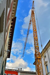 Low angle view of crane by building against sky