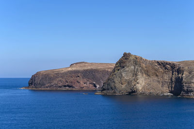 Rock formations by sea against clear blue sky