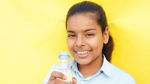 Portrait of young woman holding bottle against yellow background