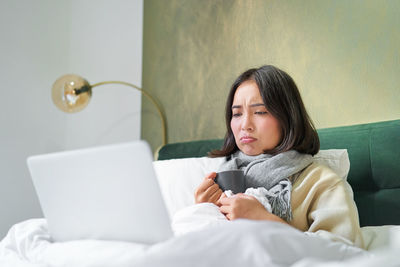 Young woman using mobile phone while lying on bed at home