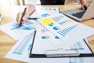 Midsection of businessman pointing at graph while using laptop at table in office