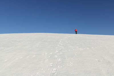 Woman on snow covered land against clear blue sky