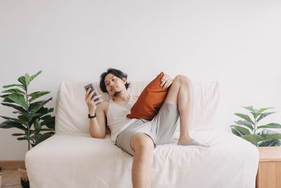 Full length of man using mobile phone lying on bed at home