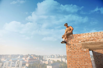 Low angle view of man standing by building against sky