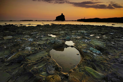 Rocks on sea shore against sky during sunset