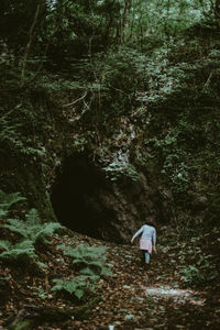 Wide angle view of young girl approaching the mouth of a cave in the forest