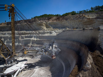 Earth mover on mining mountain against cloudy sky