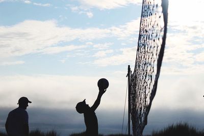 Silhouette of men with arms raised against cloudy sky