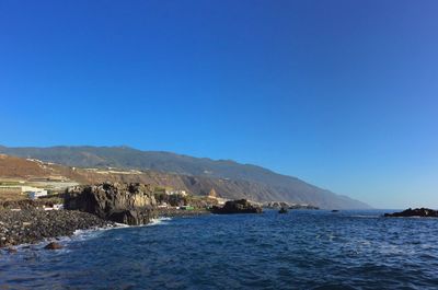 Scenic view of sea and mountains against clear blue sky