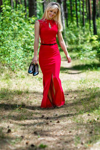 Full length of woman holding shoes while walking in forest