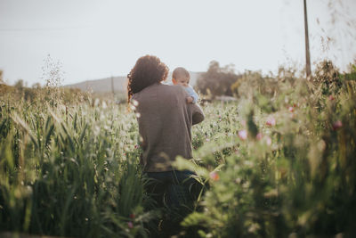 Rear view of woman with baby walking on field against sky