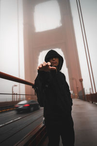 Man reaching while standing on bridge in city