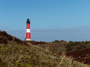 Lighthouse on field by sea against sky