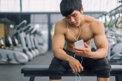 Shirtless muscular man using mobile phone in gym