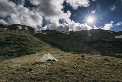 Tent on mountain against cloudy sky during sunny day