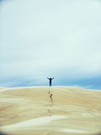Woman with arms outstretched standing on desert against sky