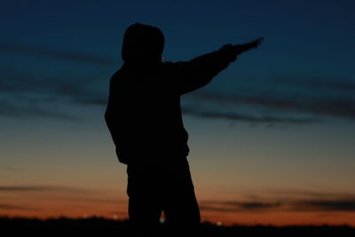 Silhouette boy standing against sky during sunset