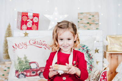 Happy little girl at home holding toy camera wearing red christmas dress at home over christmas deco