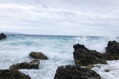 Water splashing in sea against cloudy sky