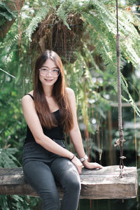 Portrait of young woman sitting against plants