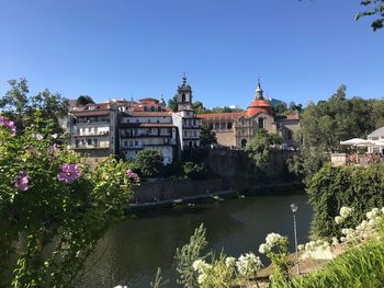 View of buildings by river against blue sky