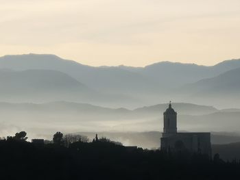 Silhouette of building and mountains against sky