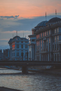 Bridge over river against buildings in city during sunset