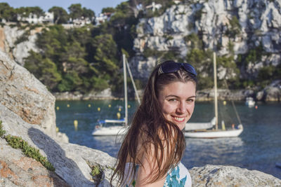 Portrait of smiling beautiful woman by rock formation with yacht on river in background