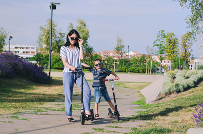 Happy family lifestyle. mother, boy, girl walking in city. ride scooters. laughing on summer. fun