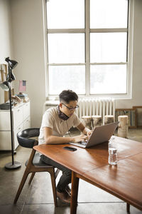 Businessman wearing headphones using laptop at table in creative office