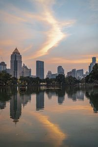 Reflection of buildings in city against sky during sunset