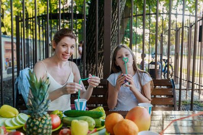 Portrait of smiling mother and daughter with fruits on table