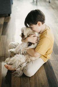 Boy embracing dog sitting on floor at home
