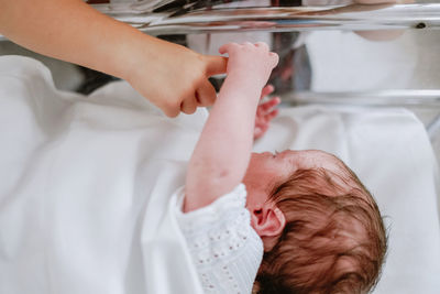 Little girl standing near newborn baby sibling sleeping in hospital cradle in ward